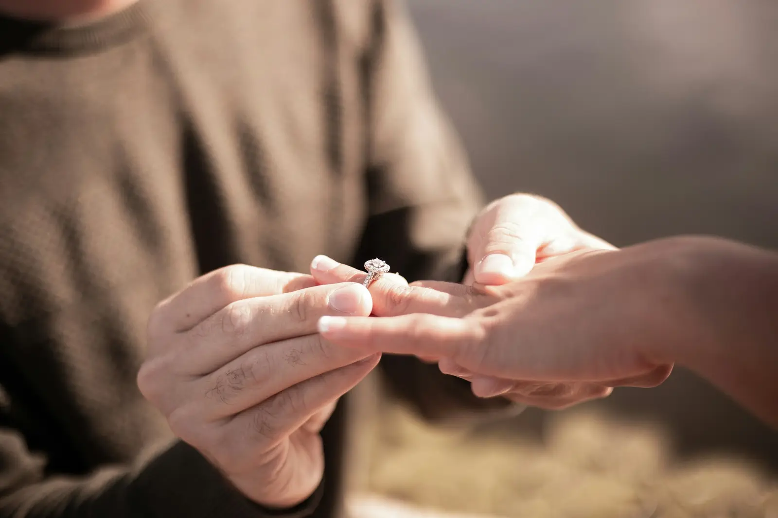 A man kneeling to propose on a riverside path as his partner covers her mouth in surprise
