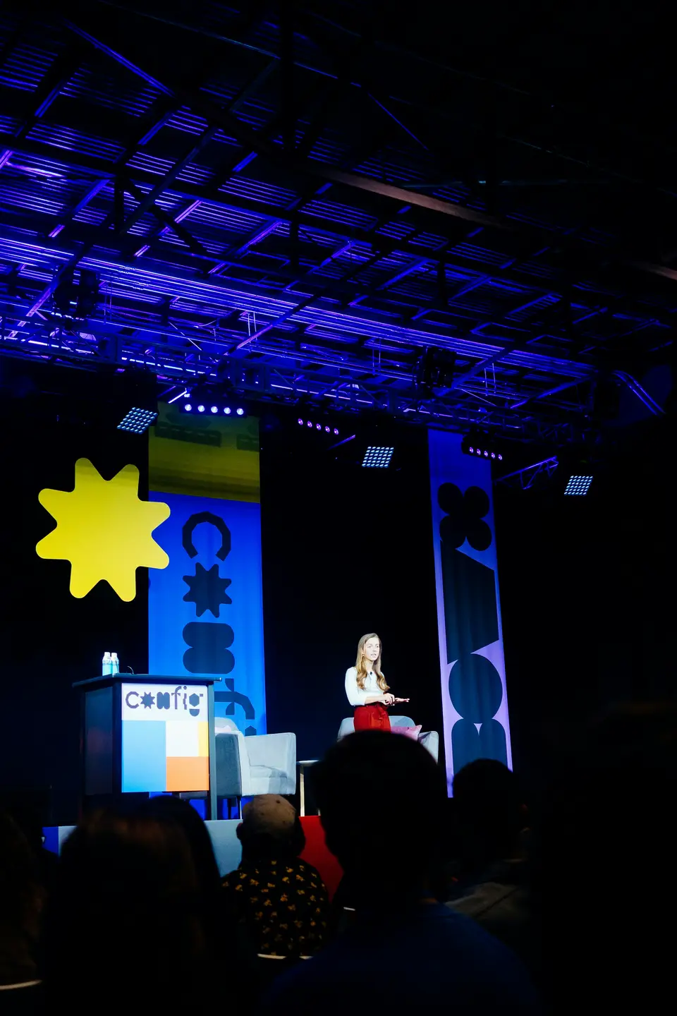 A speaker presenting to a conference audience in front of a branded screen