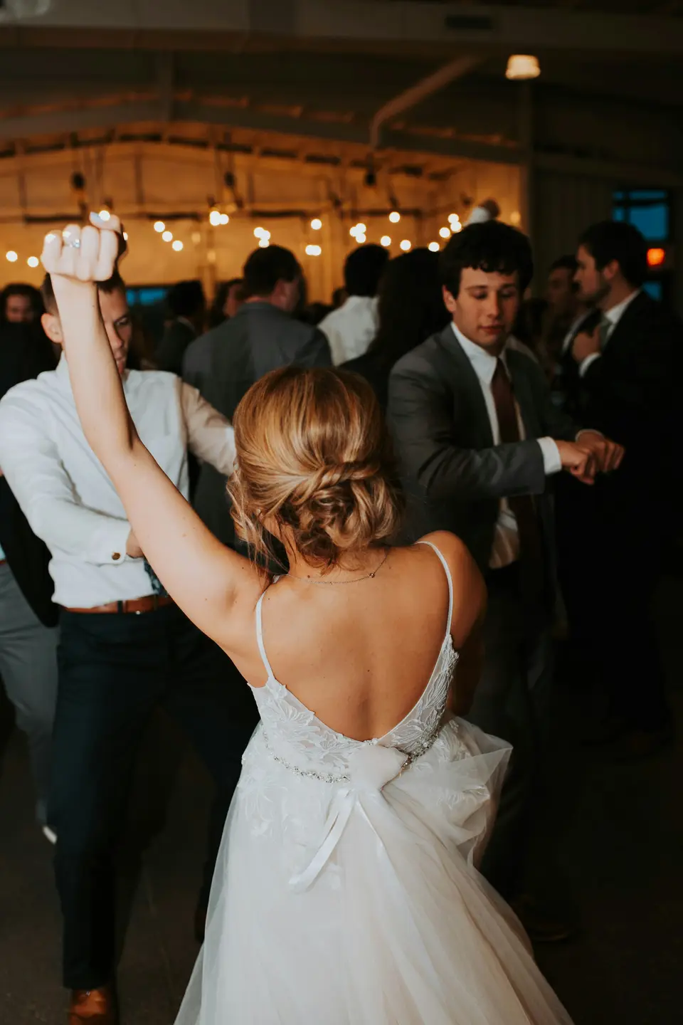 A couple sharing their first dance under festoon lights in a barn